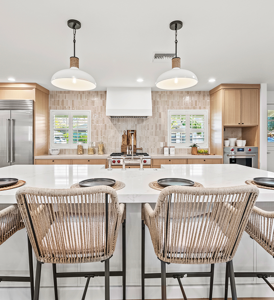 Modern kitchen with wooden stools and pendant lights over a white island.